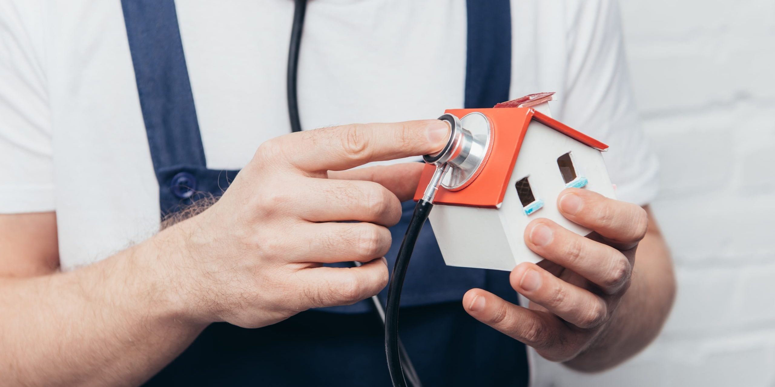 cropped shot of craftsman checking house figure by stethoscope, home inspection concept
